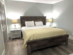 Een slaapkamer met een houten bedframe, witte beddengoed, twee nachtkastjes met lampen, en een houten vloer.