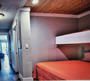 A room with a bunk bed, a door, and a hallway leading to another room.