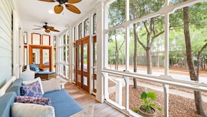 A covered porch with a blue sofa, white railings, and a ceiling fan.