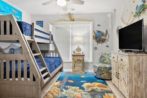 Cozy bedroom with a bunk bed, bedside table, and TV cabinet, featuring a fun fish-themed carpet and wall mural.