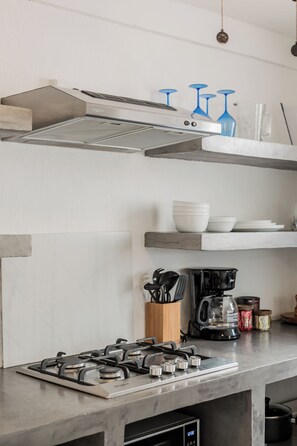 A kitchen with a gas stove, coffee maker, and shelves with dishes and utensils.