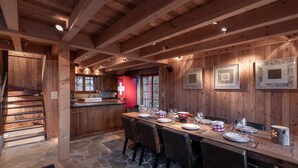 A wooden interior with a stone floor, a dining table set for six, and a staircase leading to a lower level.