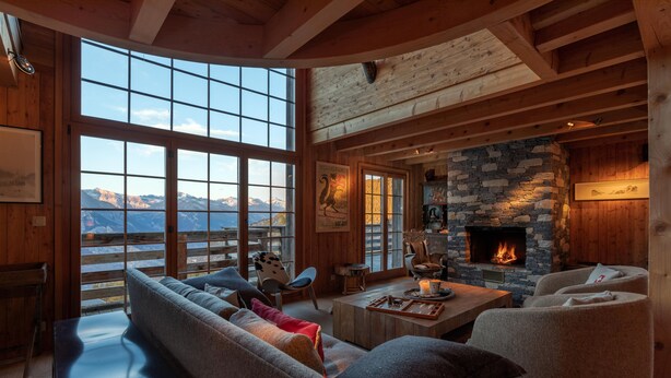 A cozy living room with a stone fireplace, large windows, and a view of mountains.