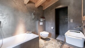 A modern bathroom with a stone floor, a freestanding bathtub, a toilet, and a shower.