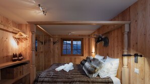 A wooden cabin room with a bed, a shelf with boots, a window with a mountain view, and a mounted animal head.