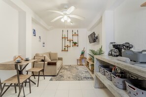 A modern kitchen with a dining area, wooden furniture, a ceiling fan, and a TV mounted on the wall.