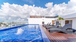 Ein Pool auf dem Dach mit Blick auf die Stadt, Liegestühle und eine Holzterrasse.