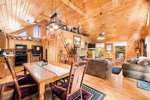 A wooden cabin interior with a dining area, kitchen, and living room. - Heaven’s Window - Luxury Log Home - Amazing Views (Sevierville)