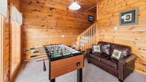 Habitació acollidora amb sostre de fusta, taula de futbolí, sofà de cuir marró i una escala.
