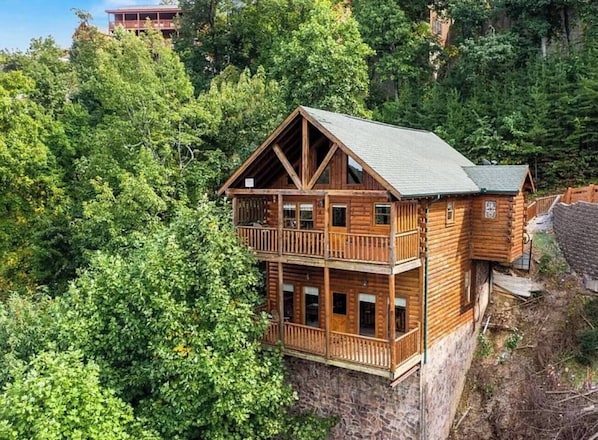 A multi-story wooden cabin with balconies, surrounded by dense forest.