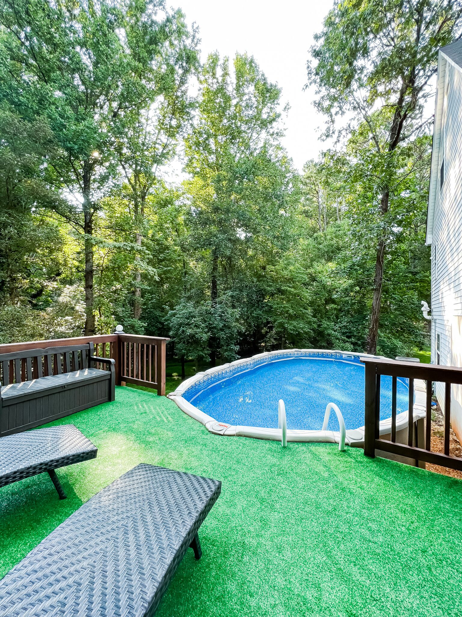 Un jardin avec une piscine, entouré d’arbres et doté d’une terrasse en bois avec des sièges.