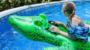 Eine Person im Pool mit einem grünen, aufblasbaren Krokodil-Schwimmtier.