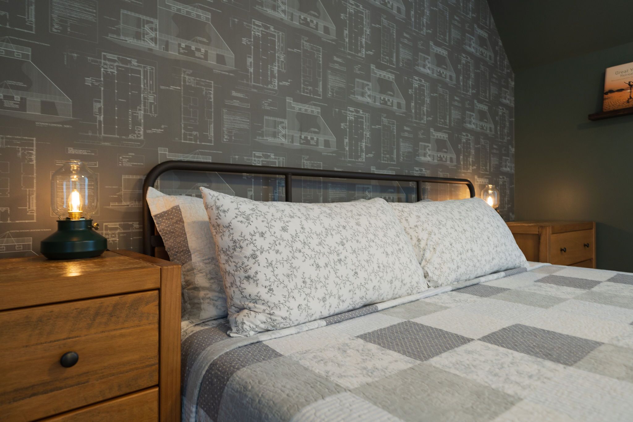 Un dormitorio con una cama, una mesita de noche y una pared con dibujos arquitectónicos.