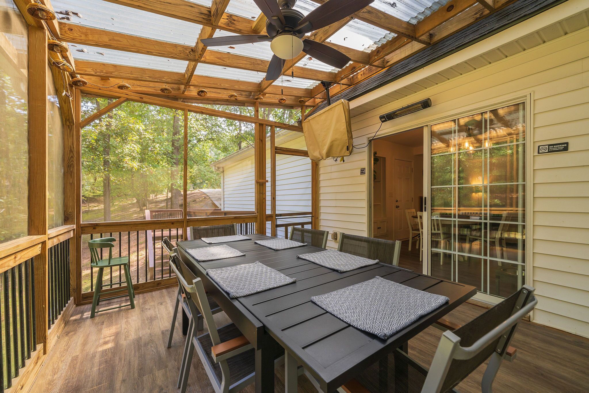 A covered outdoor dining area with a table set for four, surrounded by chairs, and a ceiling fan above.