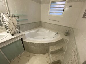 A bathroom with a large bathtub, a glass shower enclosure, and a small window. - Villa Sea View (Saint-Leu)
