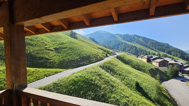 A view of a road curving through green hills with buildings on the right. - Apartment La Foux Heated pool access (La Foux d'Allos)