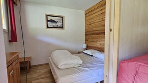 A bedroom with a wooden headboard, a bed with white bedding, a nightstand with a lamp, and a framed picture on the wall. - Apartment La Foux Heated pool access (La Foux d'Allos)