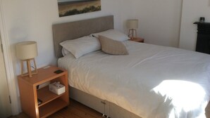Et soveværelse med en seng, to sengeborde med lamper, et natbord med lampe, et billede på væggen og trægulv.