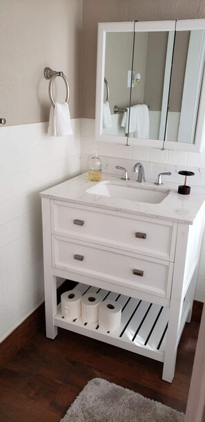 Bathroom features a vanity with drawers and a shelf, a large mirror, and a towel hanging above the sink.