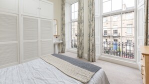 Une chambre à coucher avec un lit, une fenêtre avec des rideaux, une commode et une vue sur les bâtiments à l’extérieur.