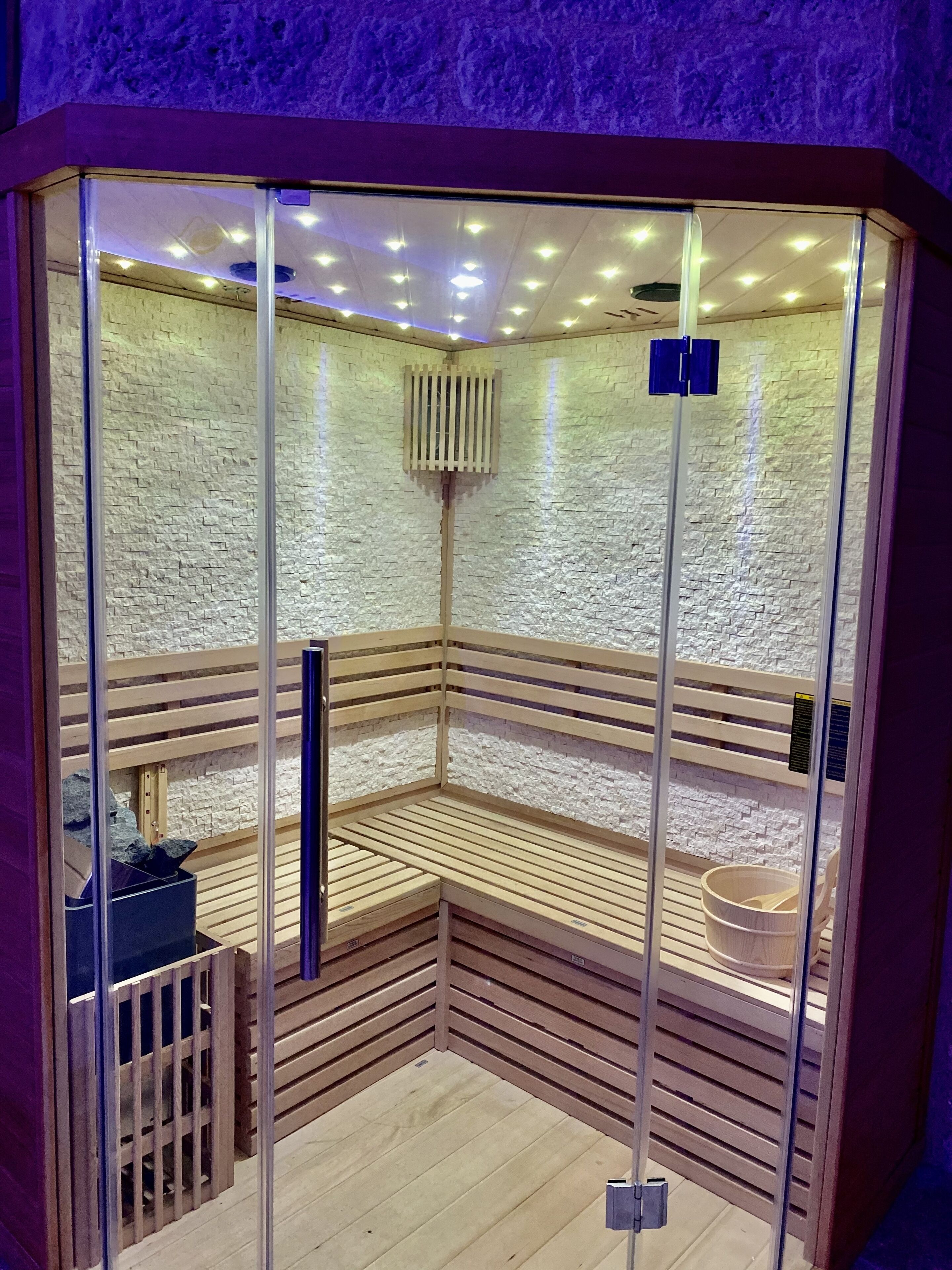 Un sauna avec un banc en bois, un mur en pierre et une paroi en verre.