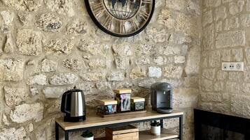 Un mur en pierre avec une horloge ronde, une machine à café et une bouilloire, le tout posé sur une console en bois.