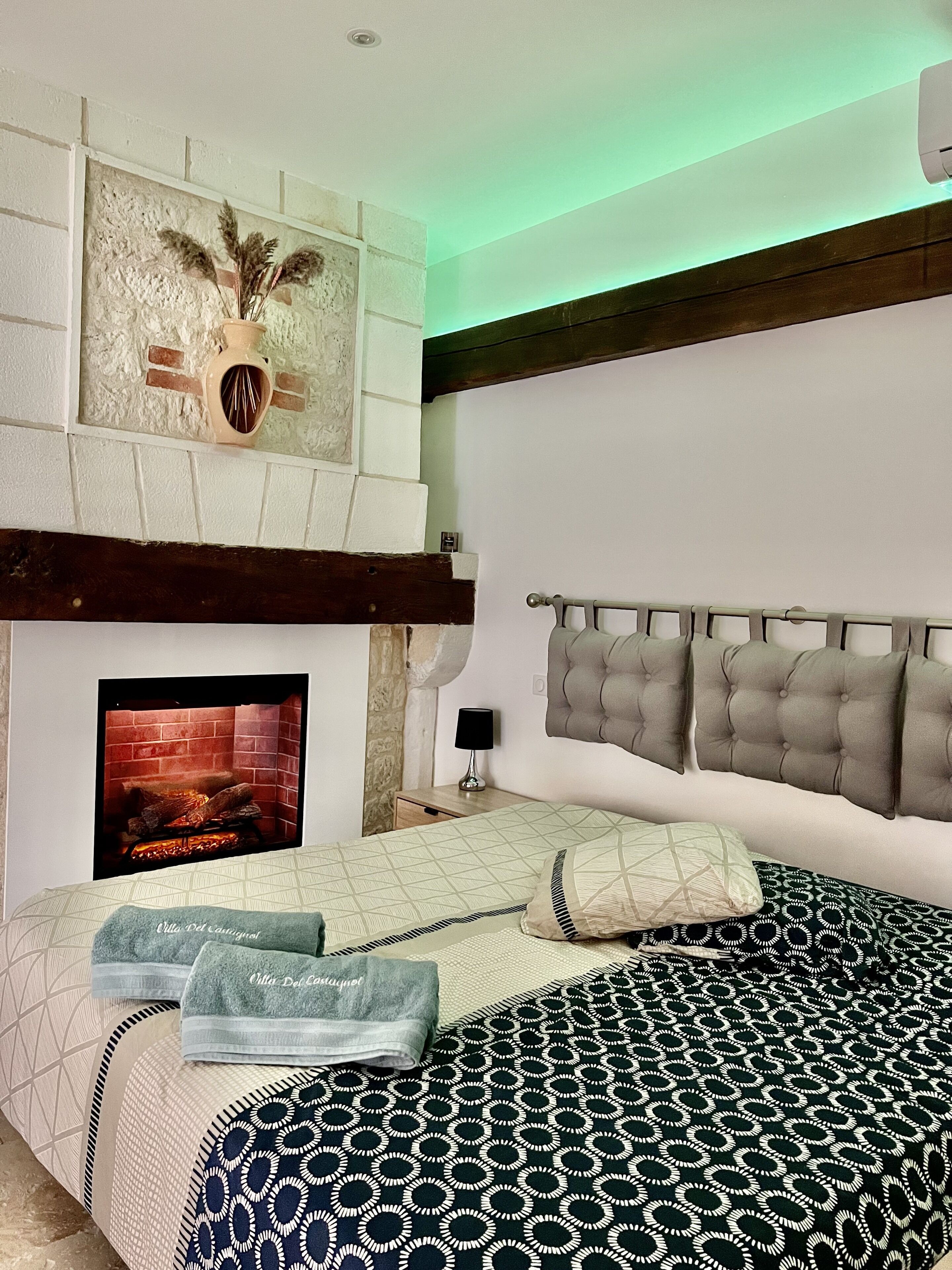 Une chambre à coucher avec un lit, une cheminée, un téléviseur fixé au mur et une table de chevet.