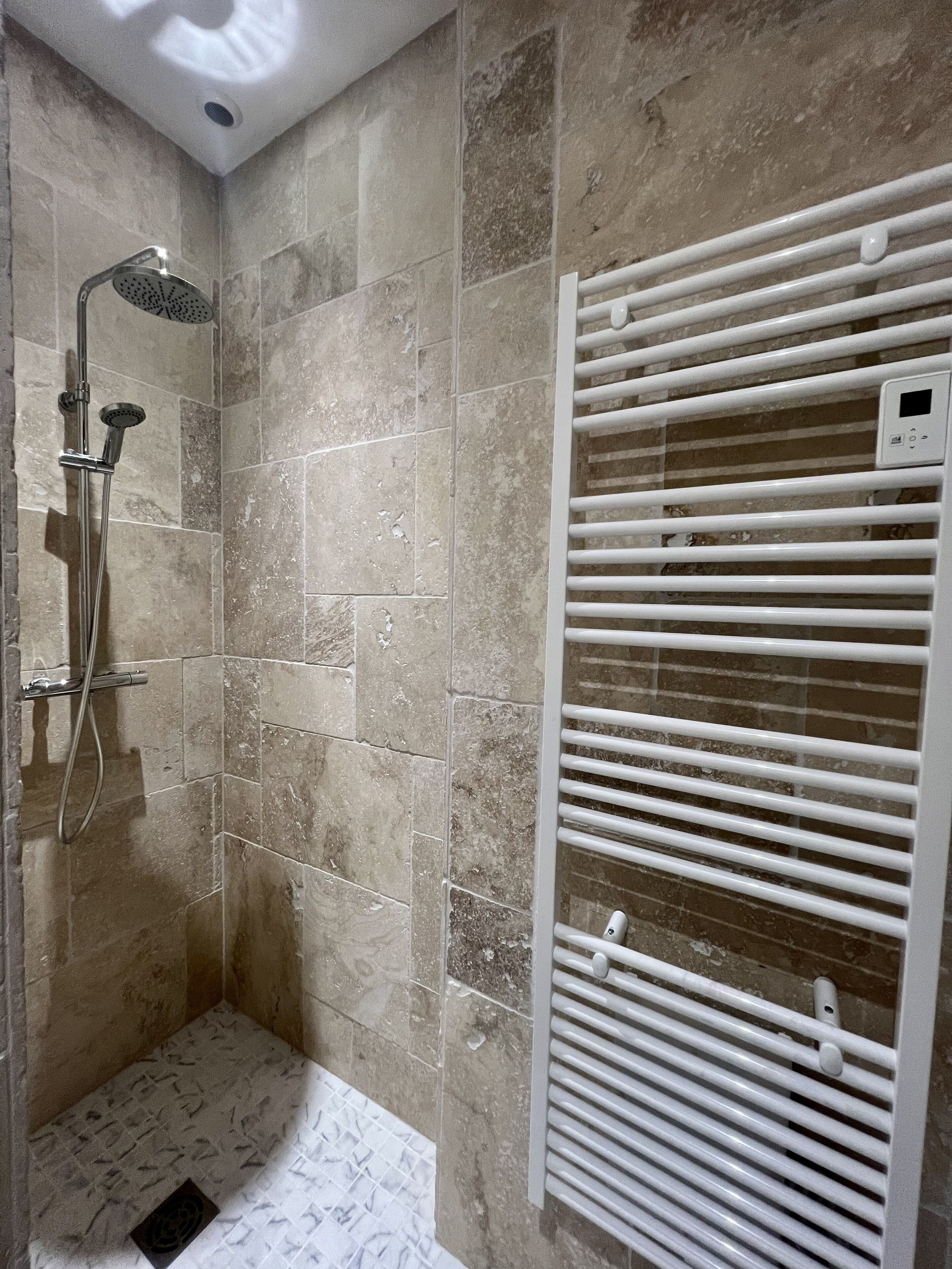 A shower with a handheld showerhead and a wall-mounted control panel.