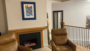 A living room with a fireplace, two leather chairs, a framed picture, and a wooden floor.