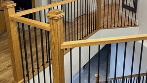 A multi-level interior with wooden railings, a fireplace, and a hallway leading to a door.