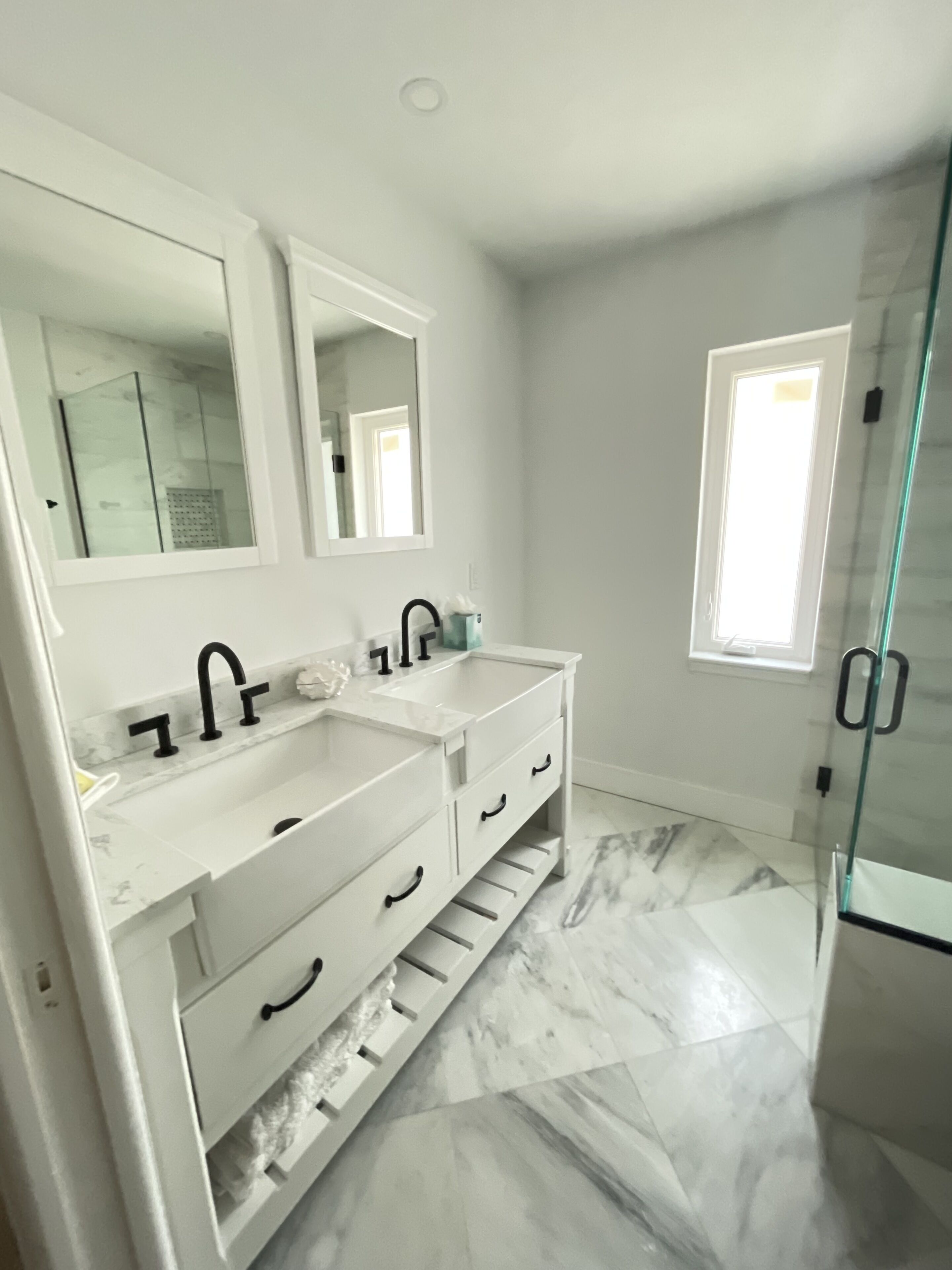 A modern bathroom with two sinks, a large mirror, and a glass shower enclosure.