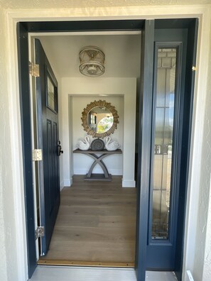 A hallway with a dark door, a light-colored wall, a decorative mirror, and a small table with swan-shaped vases. - Marco Island House Walk Distance to Beaches (Marco Island)