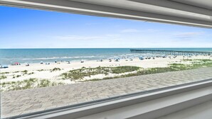 A beach view from a window overlooking a sandy beach with a pier extending into the water.