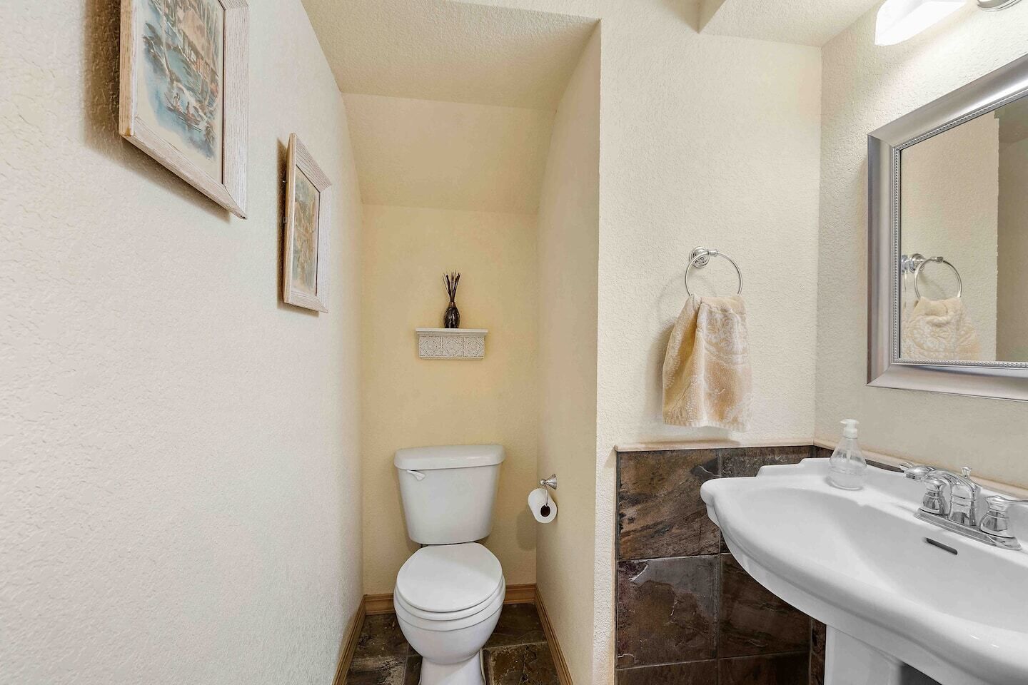 Une salle de bain avec des toilettes, un lavabo et un miroir. Une serviette est accrochée au mur, et une petite étagère contient un objet décoratif.