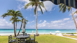 Zona pranzo all'aperto tropicale con vista sull'oceano, palme e spiaggia.