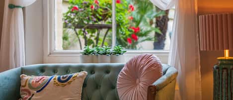 Una habitación acogedora con un sofá color turquesa, una mesita con una lámpara y una ventana con cortinas.
