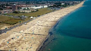 Oversigtsbillede af en strand med promenade, bygninger og en klar himmel.