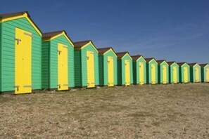 A row of beach huts with a simple, functional design, featuring a flat roof and a single door on each.