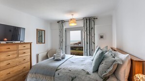 A bedroom with a bed, a wooden dresser, a television, and a window with curtains. - Sea View 3 Bedroom Seaside Property (Chichester)