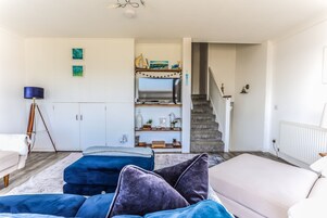 Uma sala de estar com sofá, mesa de centro, luminária, escada e estante de livros.