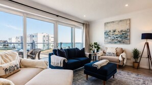 A modern living room with a large window, a blue sofa, a beige sofa, and a floor lamp. - Sea View 3 Bedroom Seaside Property (Chichester)