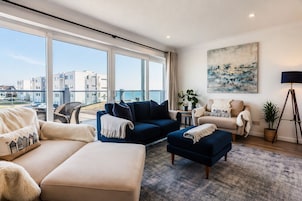 Uma sala de estar moderna com uma janela grande, um sofá azul, um sofá bege e um abajur.