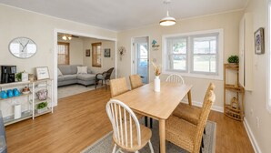 A dining area with a wooden table and chairs, a coffee station, and a living room with a sofa and a clock. - Ocean View- 5 min Walk to Beach, Volleyball (Kill Devil Hills)