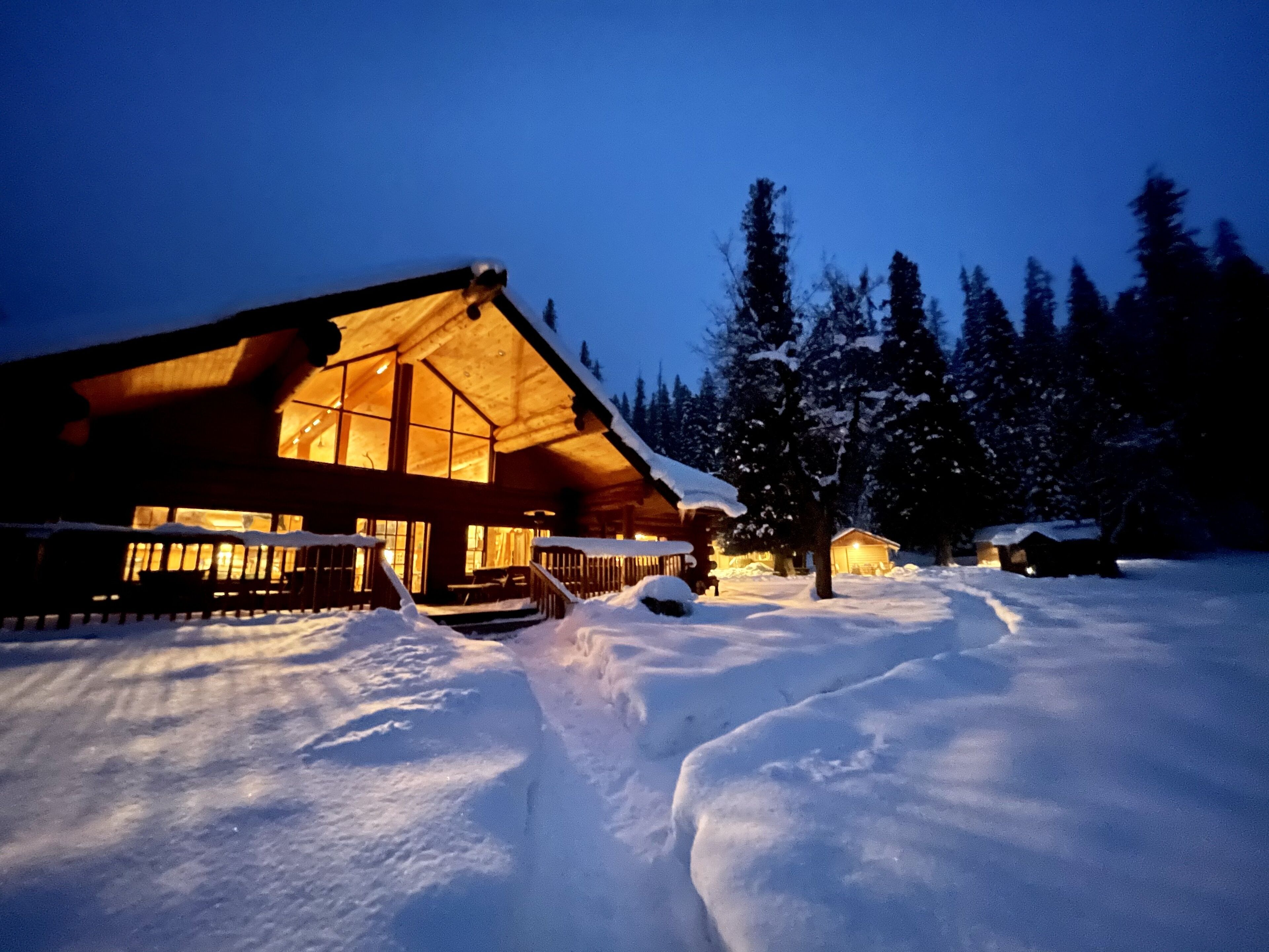 A log cabin with a large porch and a snow-covered landscape at night.