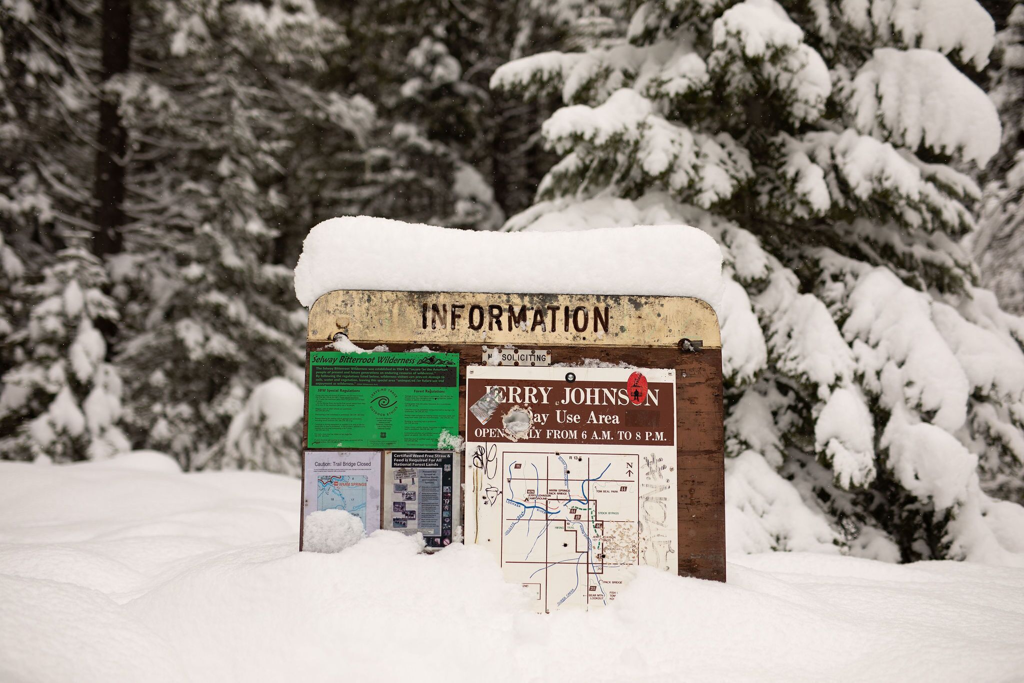 Un panneau d’information recouvert de neige, avec une carte et un panneau vert.