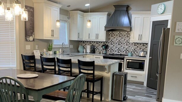 A modern kitchen with white cabinets, a central island, and a dining area with green chairs.