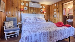 Une pièce aux murs lambrissés, contenant un lit, une chaise et un lavabo.