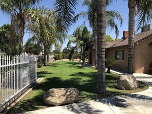 Stucco house with a brick chimney, surrounded by a well-manicured lawn and palm trees, set behind a white picket fence.