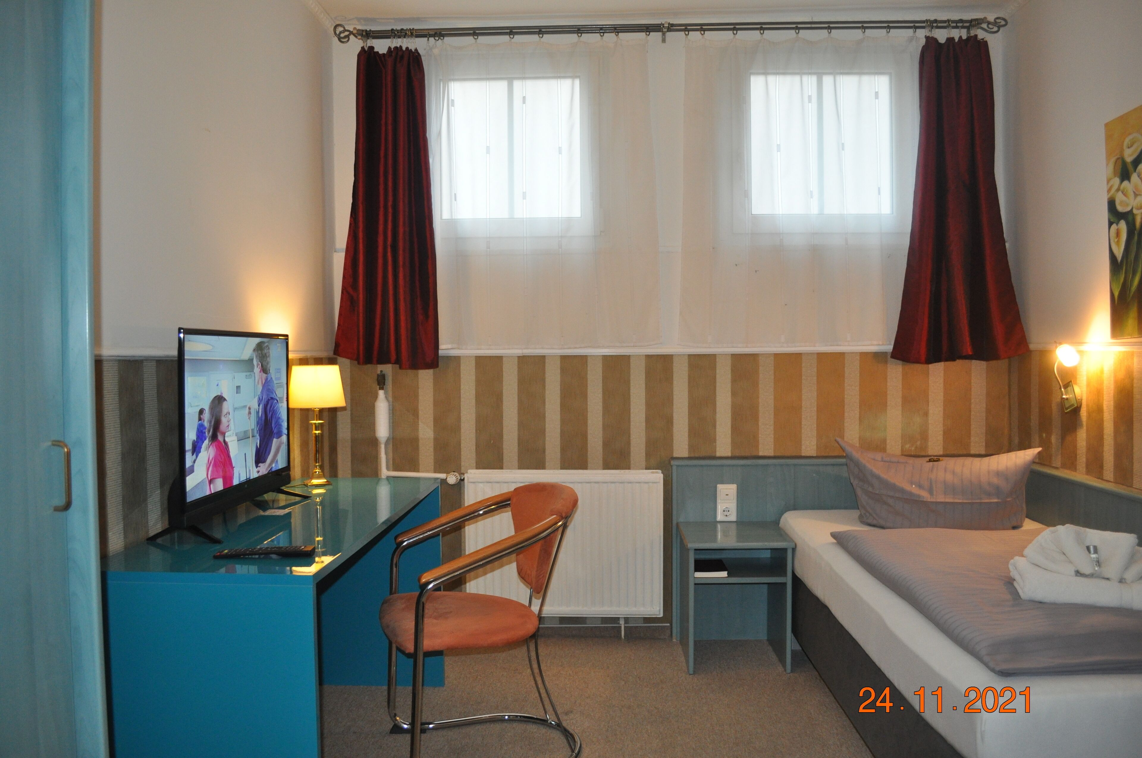 Habitación de hotel con cama, escritorio, monitor de computadora, silla, una mesita y ventana con cortinas.