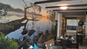 Un restaurante con un mural de un árbol junto a un lago, asientos de piedra y vistas al comedor.